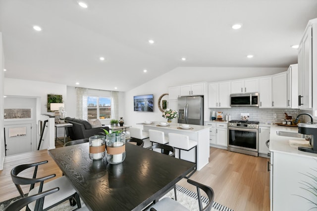 dining area featuring sink, vaulted ceiling, and light wood-type flooring