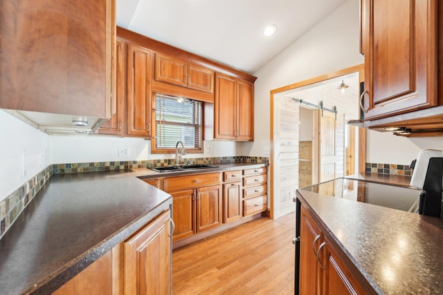 kitchen with a barn door, sink, lofted ceiling, and light wood-type flooring