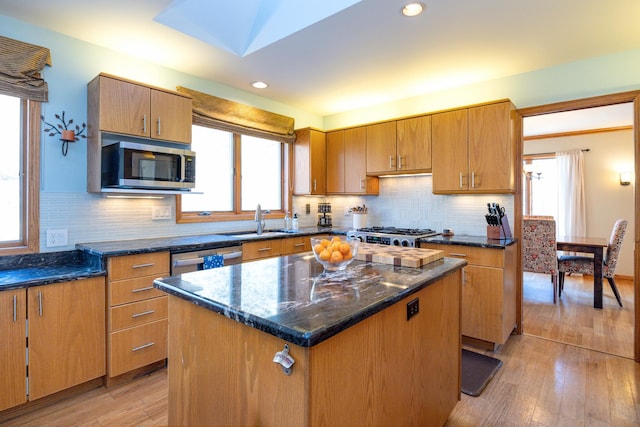 kitchen featuring a kitchen island, sink, light wood-type flooring, stainless steel appliances, and dark stone counters