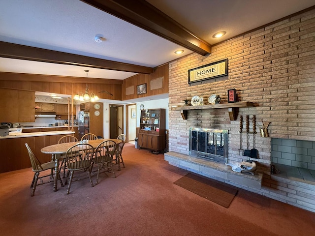 dining area featuring a notable chandelier, a fireplace, beamed ceiling, and dark colored carpet