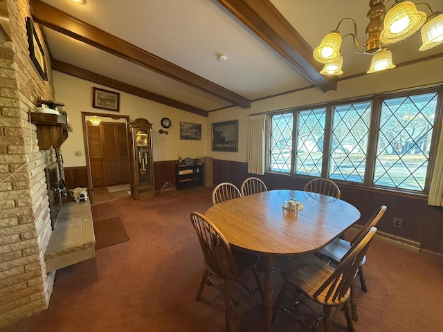 dining space with wood walls, lofted ceiling with beams, dark colored carpet, a notable chandelier, and a brick fireplace