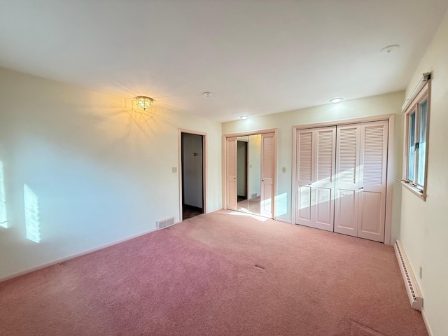 unfurnished bedroom featuring baseboard heating, multiple closets, and carpet floors