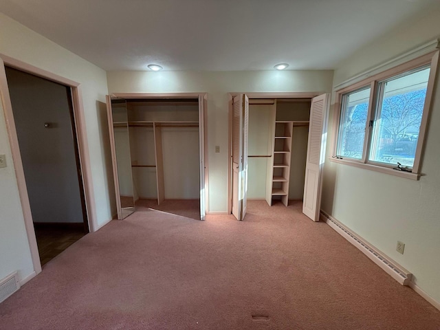 unfurnished bedroom with a baseboard heating unit, two closets, and carpet flooring