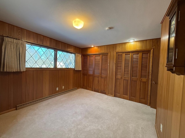 unfurnished bedroom with a baseboard heating unit, carpet floors, a textured ceiling, two closets, and wood walls