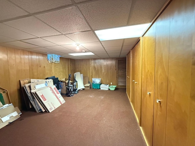 basement with a drop ceiling and wood walls