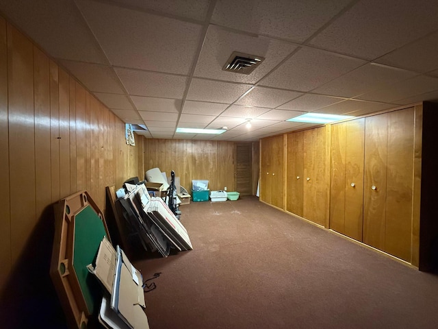 basement with a paneled ceiling, wooden walls, and carpet