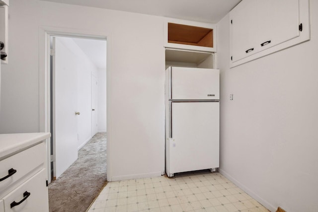 kitchen with white cabinetry, white refrigerator, and light carpet