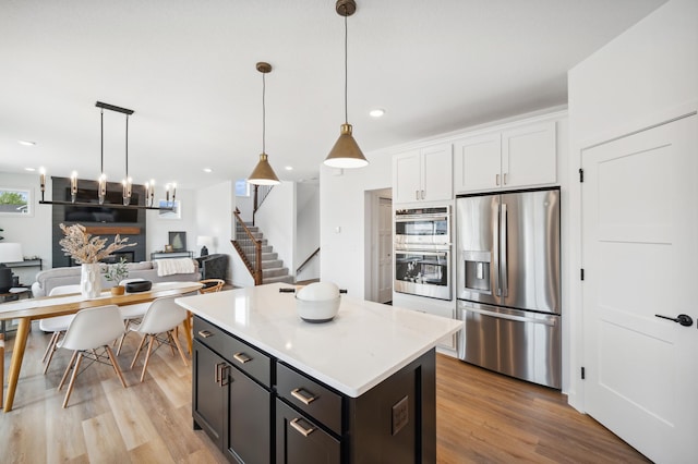 kitchen featuring decorative light fixtures, a center island, light hardwood / wood-style flooring, stainless steel appliances, and white cabinets