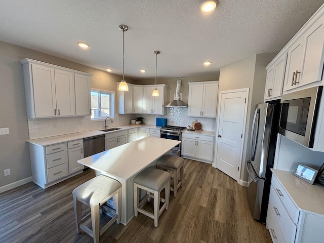 kitchen featuring white cabinetry, wall chimney range hood, pendant lighting, and stainless steel appliances