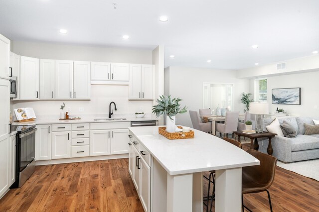 kitchen with appliances with stainless steel finishes, white cabinetry, sink, a breakfast bar area, and hardwood / wood-style flooring