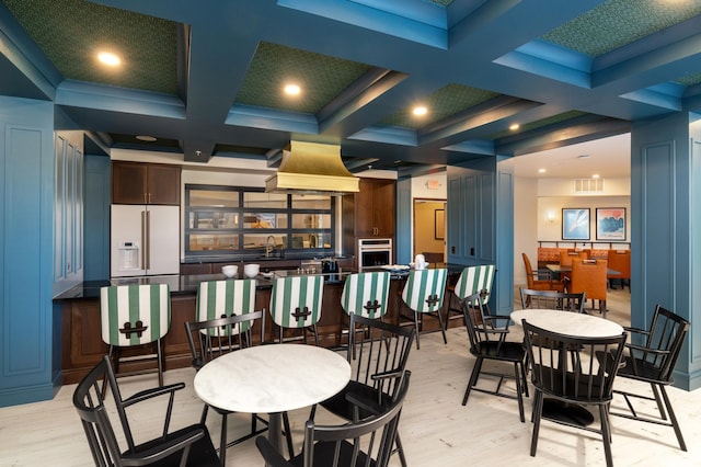 dining room with beamed ceiling, coffered ceiling, and light hardwood / wood-style flooring