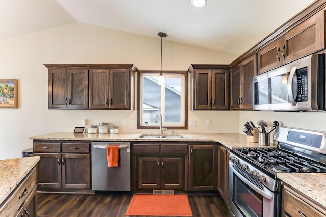 kitchen with appliances with stainless steel finishes, vaulted ceiling, pendant lighting, light stone counters, and sink