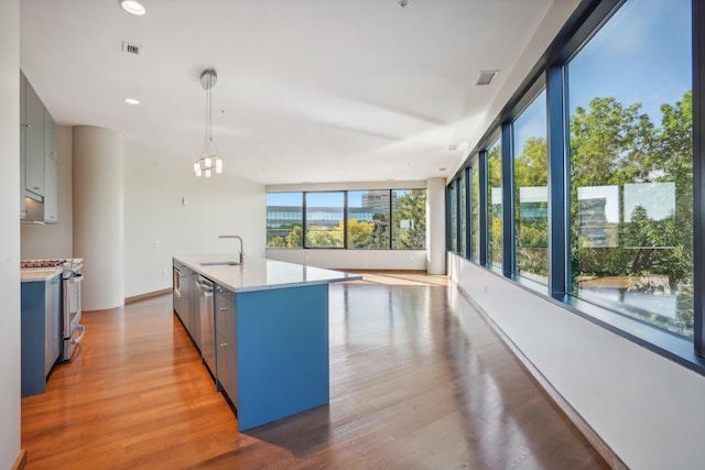 kitchen with decorative light fixtures, a center island with sink, stainless steel appliances, and a healthy amount of sunlight