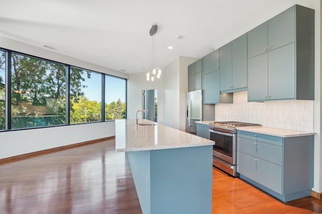 kitchen featuring pendant lighting, a center island with sink, decorative backsplash, sink, and stainless steel appliances