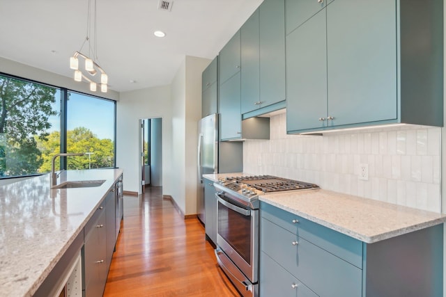 kitchen featuring stainless steel appliances, tasteful backsplash, sink, hanging light fixtures, and light hardwood / wood-style flooring