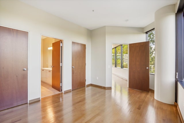 unfurnished bedroom with ensuite bath, light wood-type flooring, and multiple windows