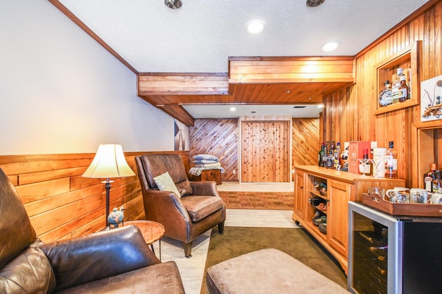 sitting room featuring carpet flooring, wine cooler, a textured ceiling, bar area, and wood walls