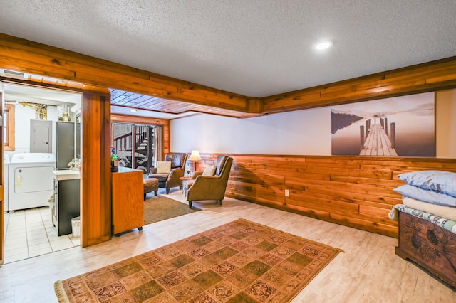 living room featuring wooden walls, electric panel, washing machine and dryer, a textured ceiling, and light hardwood / wood-style flooring