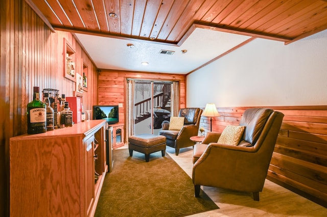 sitting room featuring ornamental molding, bar, wood ceiling, and wood walls