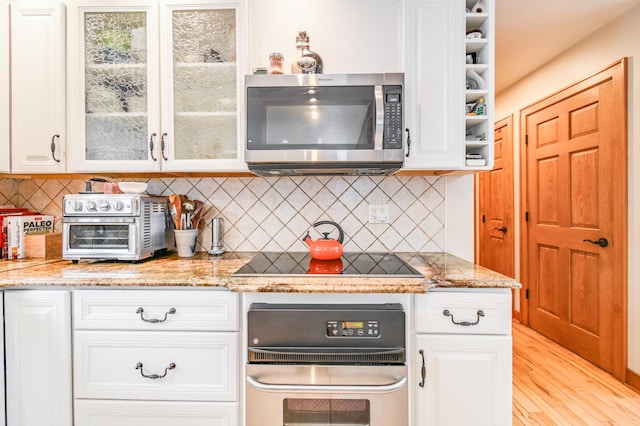 kitchen with white cabinetry, backsplash, light stone counters, and appliances with stainless steel finishes