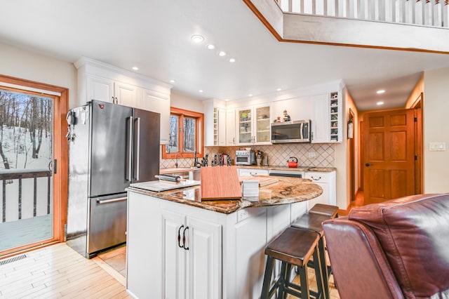 kitchen with stainless steel appliances, a center island, dark stone countertops, and white cabinets