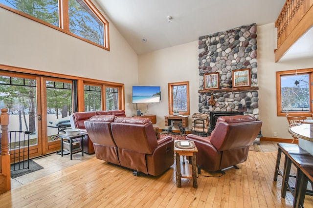 living room with a stone fireplace, high vaulted ceiling, and light wood-type flooring