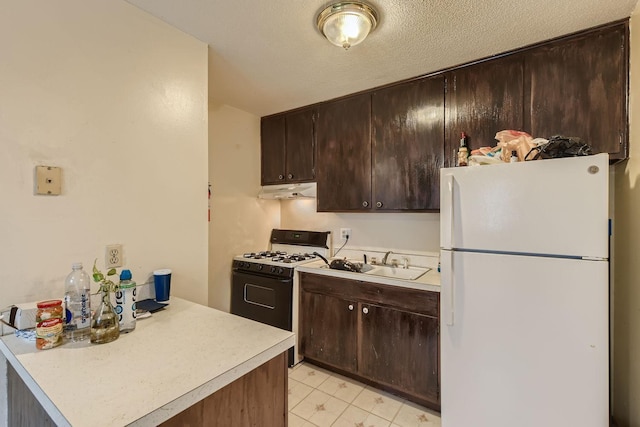 kitchen featuring light countertops, freestanding refrigerator, gas stove, dark brown cabinetry, and a sink