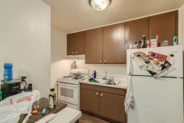 kitchen with a textured ceiling, under cabinet range hood, white appliances, a sink, and light countertops