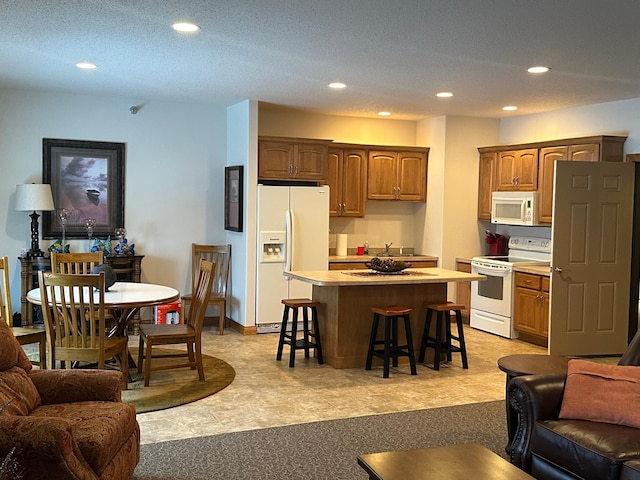 kitchen featuring a kitchen island, white appliances, a breakfast bar area, and sink