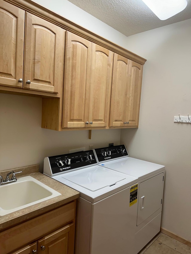 washroom with a textured ceiling, sink, washer and clothes dryer, cabinets, and light tile patterned flooring