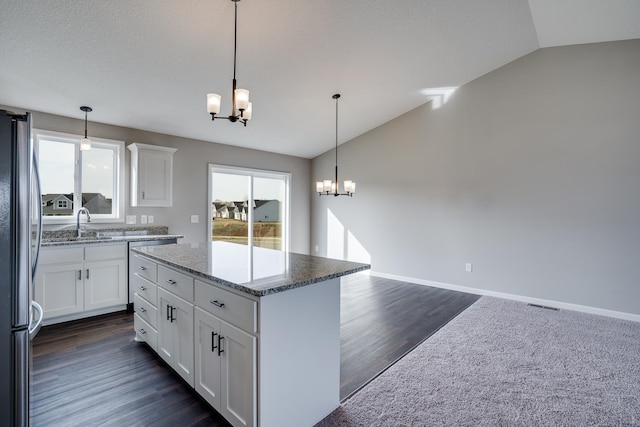 kitchen with white cabinets, a center island, lofted ceiling, stainless steel fridge, and a chandelier