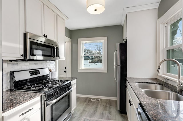 kitchen featuring white cabinets, stainless steel appliances, dark stone counters, tasteful backsplash, and sink