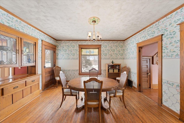 dining space with a textured ceiling, light hardwood / wood-style flooring, crown molding, and an inviting chandelier