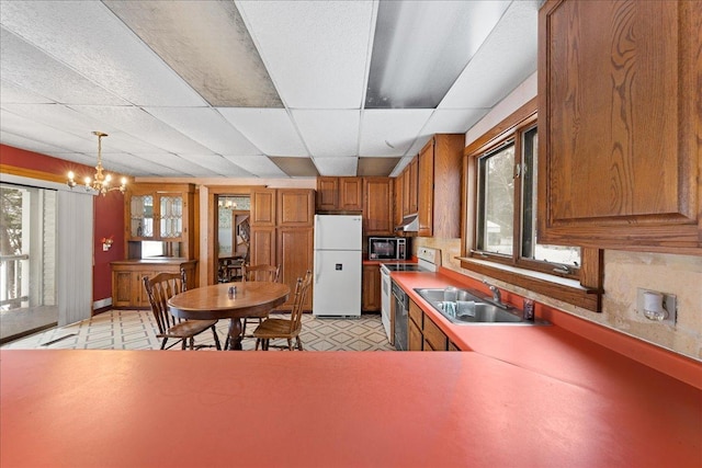 kitchen featuring sink, white appliances, hanging light fixtures, a paneled ceiling, and a chandelier