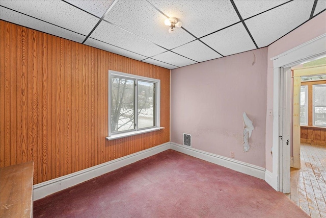 carpeted spare room featuring plenty of natural light, a paneled ceiling, and wood walls