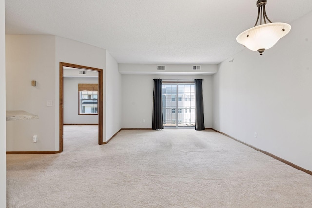 spare room featuring baseboards, light carpet, a textured ceiling, and visible vents