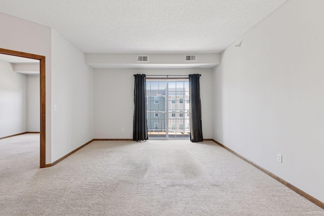 carpeted spare room with a textured ceiling, visible vents, and baseboards
