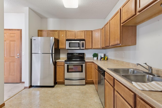 kitchen featuring brown cabinetry, light countertops, a textured ceiling, a sink, and stainless steel appliances