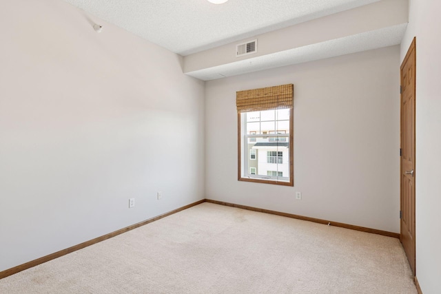 empty room with baseboards, light colored carpet, a textured ceiling, and visible vents