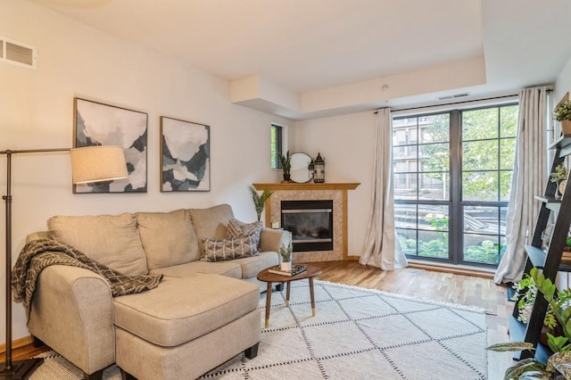 living room with a raised ceiling, light hardwood / wood-style flooring, and a tile fireplace