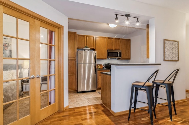 kitchen featuring stainless steel appliances, dark countertops, light wood-style flooring, brown cabinetry, and a kitchen bar