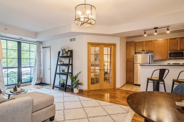 living area with french doors, visible vents, light wood-style floors, a chandelier, and baseboards