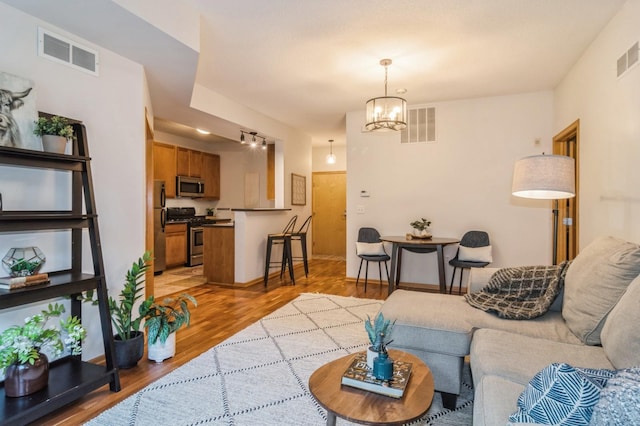 living room featuring light wood finished floors, visible vents, and a notable chandelier