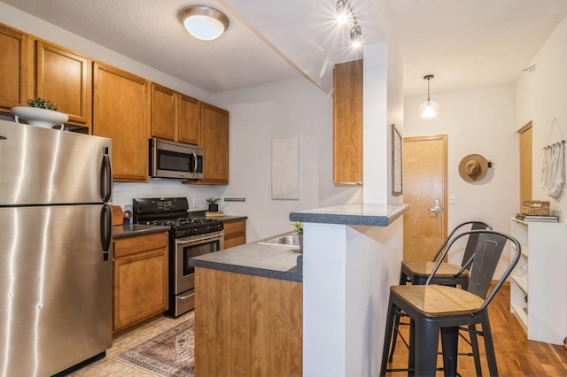 kitchen featuring a breakfast bar area, a peninsula, appliances with stainless steel finishes, brown cabinetry, and dark countertops