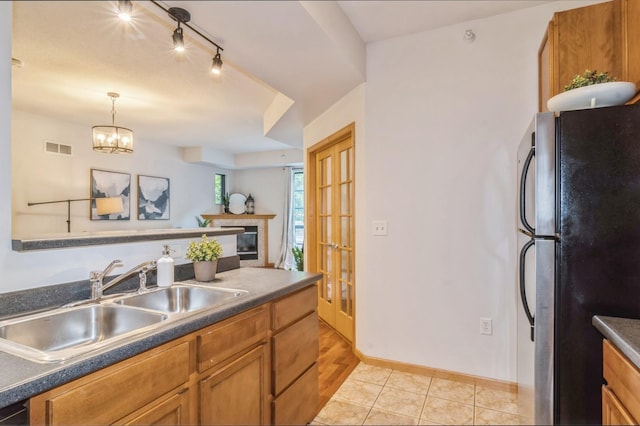 kitchen with dark countertops, visible vents, brown cabinetry, freestanding refrigerator, and a sink