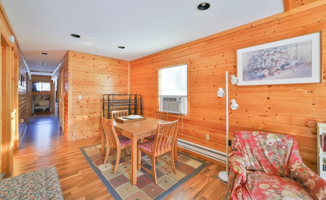 dining room featuring a baseboard heating unit, hardwood / wood-style floors, wooden walls, and cooling unit