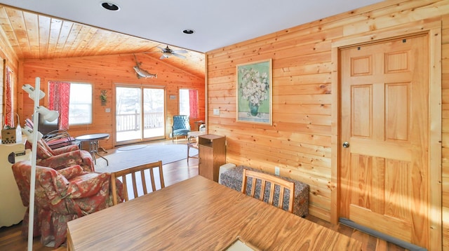 dining room with wooden walls, ceiling fan, wood finished floors, and vaulted ceiling