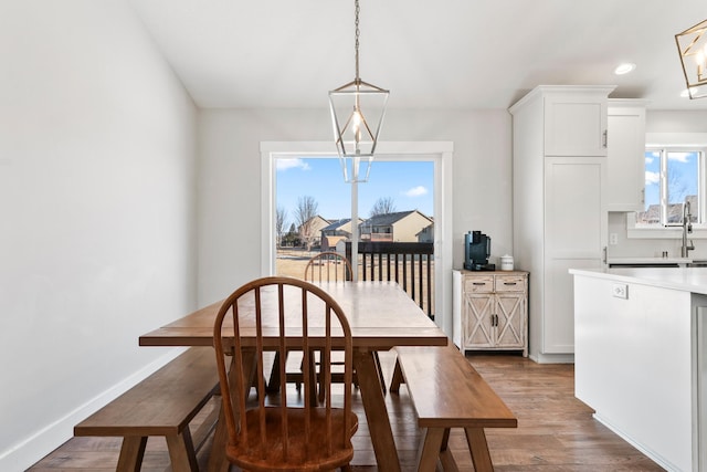 dining space with sink, wood-type flooring, and an inviting chandelier