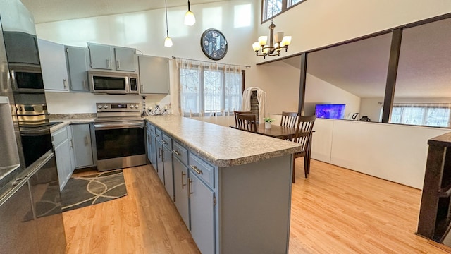 kitchen featuring kitchen peninsula, appliances with stainless steel finishes, a notable chandelier, hanging light fixtures, and light hardwood / wood-style flooring