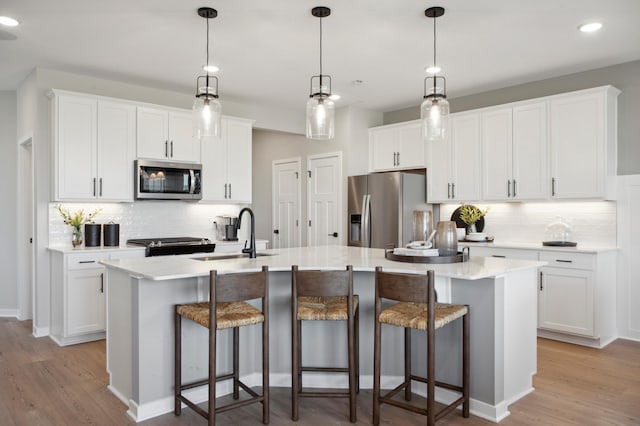 kitchen with white cabinetry, stainless steel appliances, decorative light fixtures, a kitchen island with sink, and sink